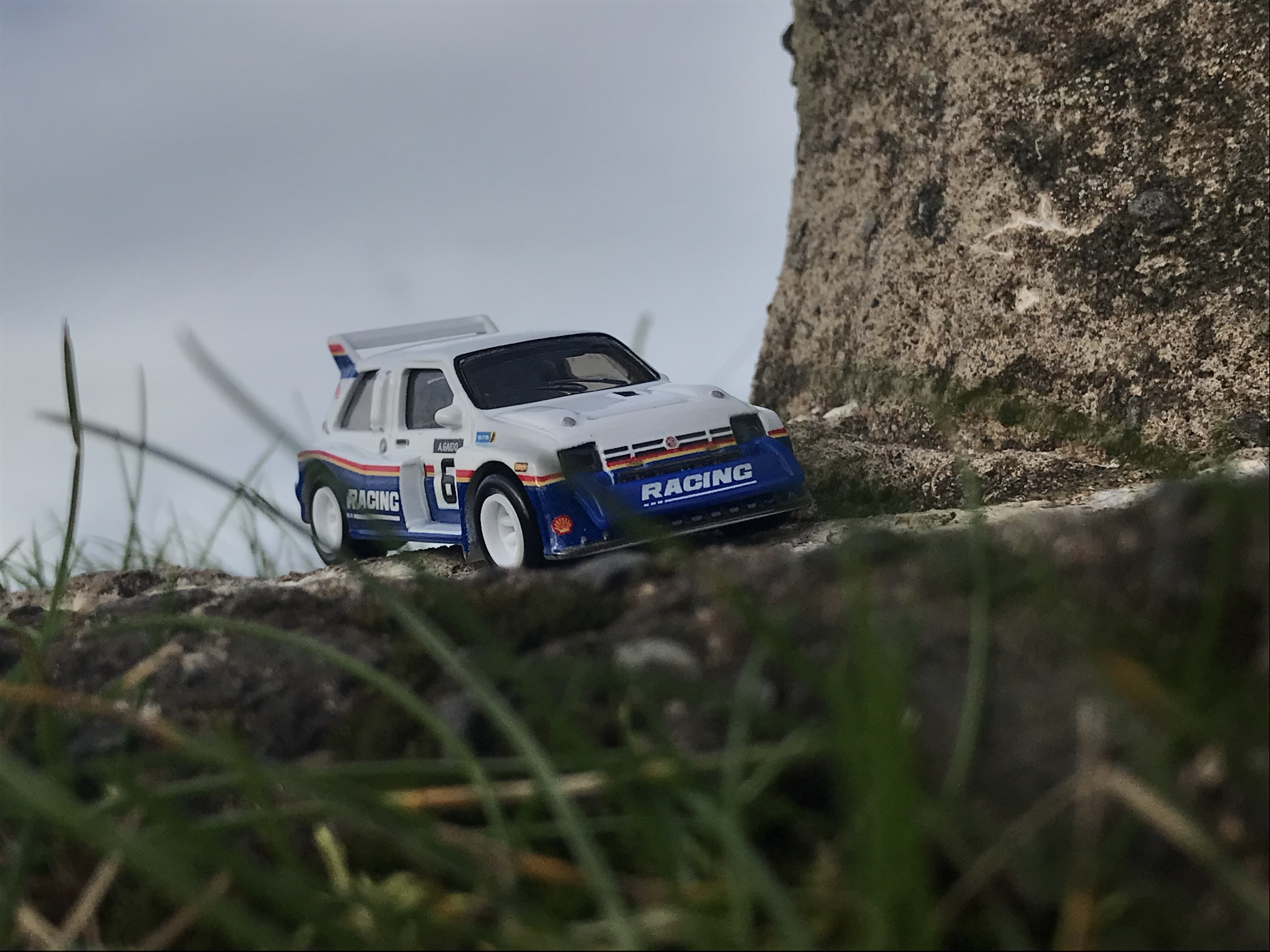 Hotwheels GrpB  Rally MG Metro 6R4 on some concrete, next to a concrete wall. Grass obscures parts of the picture, as if it was taken at ground level [Wolfs Rain OST - Stray]